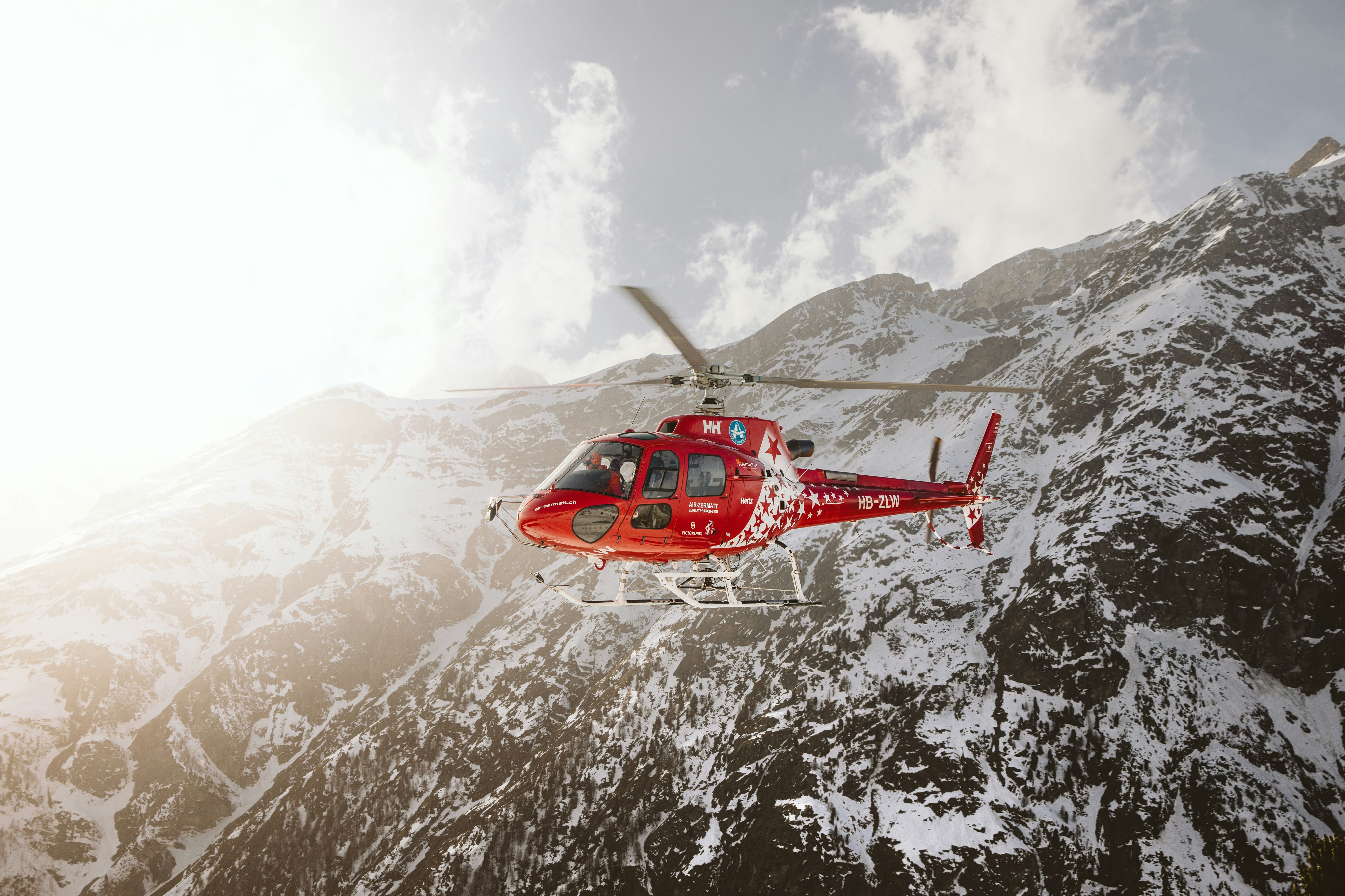 red and white helicopter flying over snow covered mountain during daytime